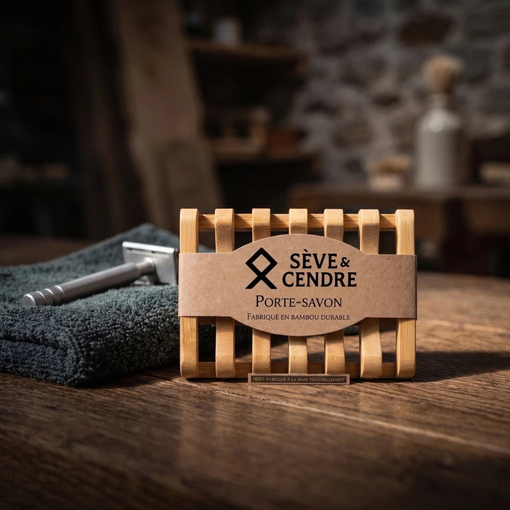 Porte-savon Sève & Cendre en bambou sur table en bois, à côté d'un rasoir de sûreté en métal et d'un linge gris.